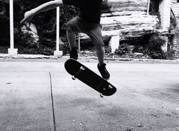 Low section of man performing stunt while skateboarding on road