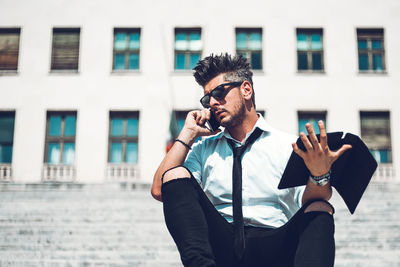 Young man wearing sunglasses standing against built structure