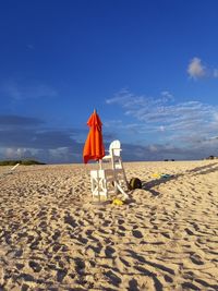 Deck chairs on sand at beach against blue sky