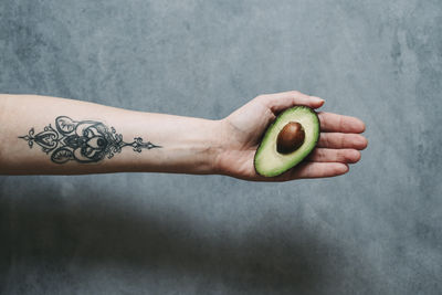 Cropped hand holding avocado against wall