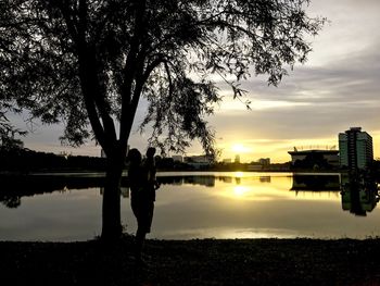 Silhouette woman standing by lake against sky during sunset