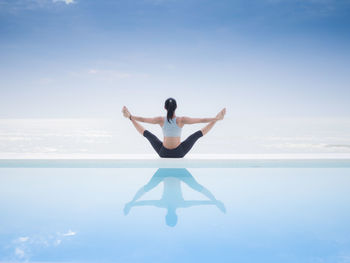 Full length of mature woman practicing yoga at poolside against sea and sky