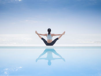 Woman practicing yoga on infinity pool by sea against cloudy sky