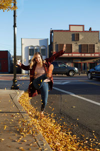 Young woman playing with autumn leaves on road in city