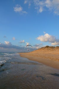 Mid distance view person paragliding over beach against sky