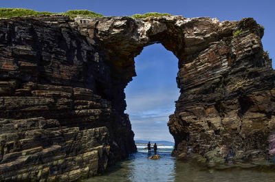 Silhouette man and woman standing amidst arch shaped of rock formation at beach