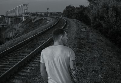 Rear view of man standing by railroad tracks