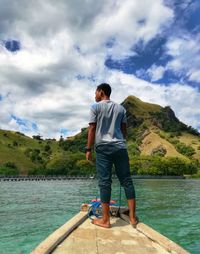 Rear view of man standing on lake against sky