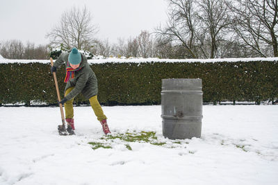 Middle-aged woman is collecting snow in a barrel with a shovel,natural resources