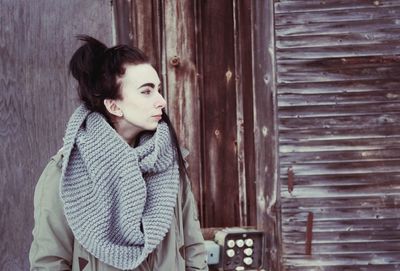 Woman looking away while standing against wooden wall during winter