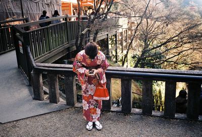 Rear view of woman with umbrella on railing against trees