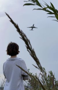 Rear view of woman looking at airplane against sky