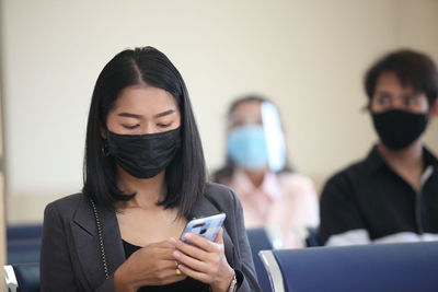Woman wearing face mask using mobile phone in waiting room