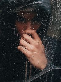 Close-up of young man seen through wet window