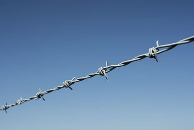 Low angle view of barbed wire against clear blue sky