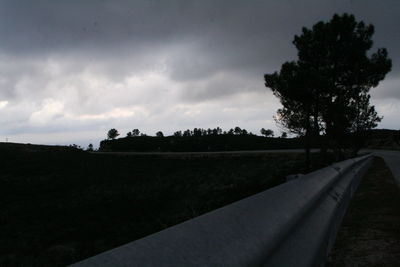 Road passing through field against cloudy sky