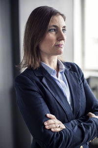 Thoughtful mature businesswoman looking away while standing arms crossed in office