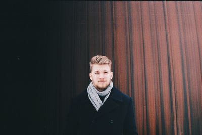 Portrait of young man standing against curtain