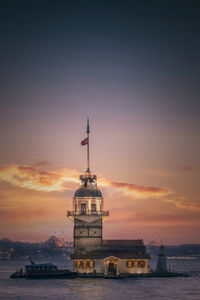 Lighthouse by sea against sky during sunset