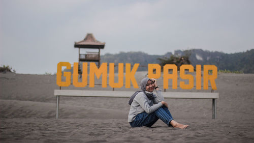 Full length of woman sitting on beach against text