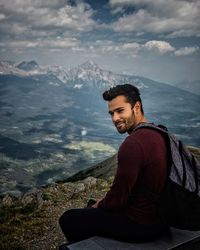 Young man sitting in sea against mountains