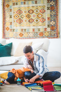 Daughter lying on busy working mother's lap in living room at home office