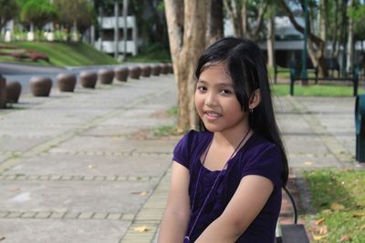 Portrait of smiling young woman sitting on footpath