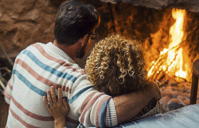 Rear view of couple sitting by fireplace
