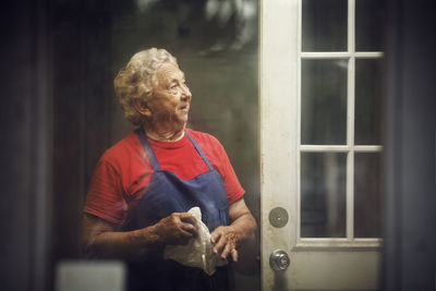 Chef looking away while standing in kitchen seen through glass