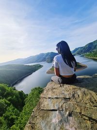 Rear view of woman sitting on rock against sky