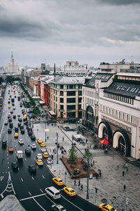 High angle view of vehicles moving on city street against cloudy sky