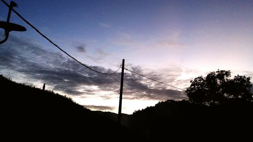 Low angle view of electricity pylon against cloudy sky