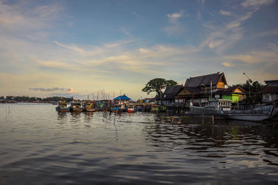 Houses by lake against sky during sunset