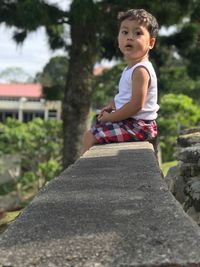 Side view of cute boy sitting on retaining wall
