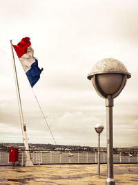 Flags on street light by sea against sky