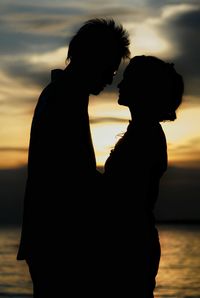 Silhouette couple standing against sea and cloudy sky during sunset