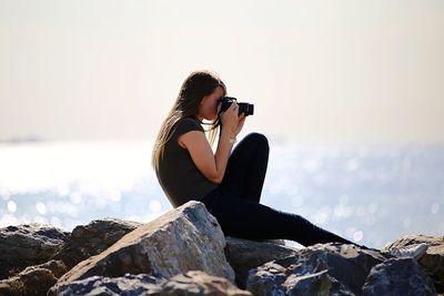 Woman sitting on rock by sea against clear sky