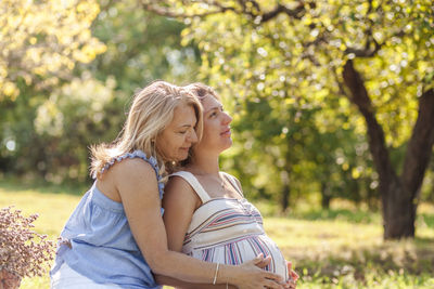 Mother embracing with pregnant daughter while sitting at park