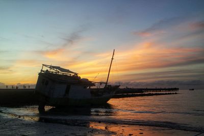 Sailboats moored on sea against sky during sunset