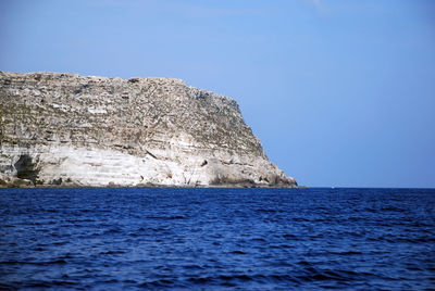 Rock formations by sea against clear blue sky