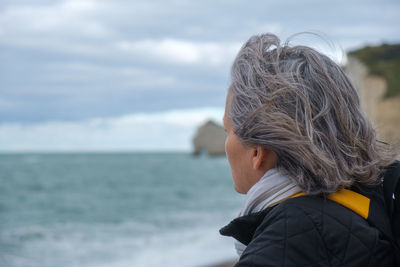 Portrait profile view of older woman with a scarf, backpack on cold beach. high quality photo