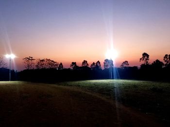 Sunlight streaming through trees on field against sky during sunset