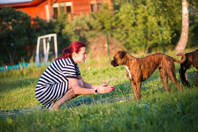 Mid adult woman playing with dog while kneeling on grassy field against sky at park