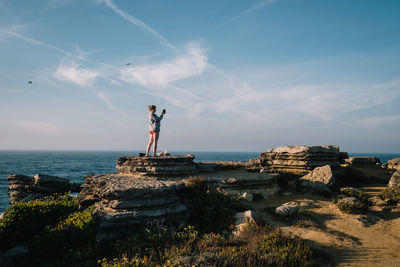 Woman standing on rock by sea against sky