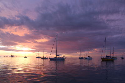 Sailboats moored in sea at sunset
