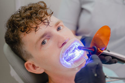 Installation of braces for a young man, an orthodontist shines ultraviolet light on the braces