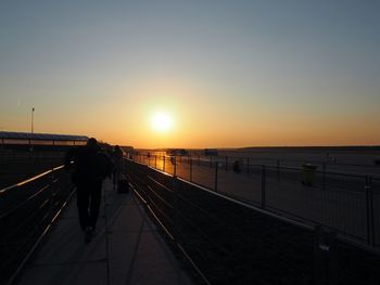 Rear view of man standing on bridge at sunset