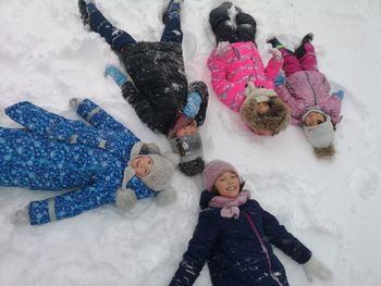 High angle portrait of cute girls lying on snow covered field