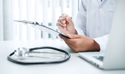 Midsection of doctor writing on clipboard