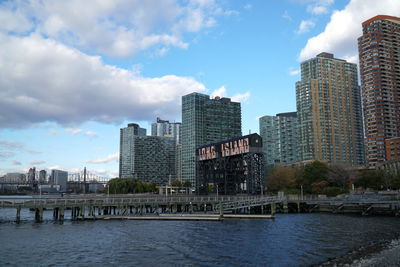 Modern buildings by river against sky in city